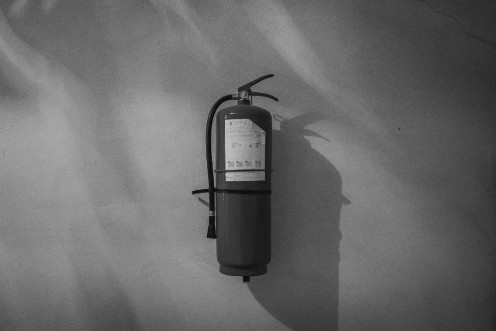 Black and white image of a fire extinguisher hung up on a plain white wall.