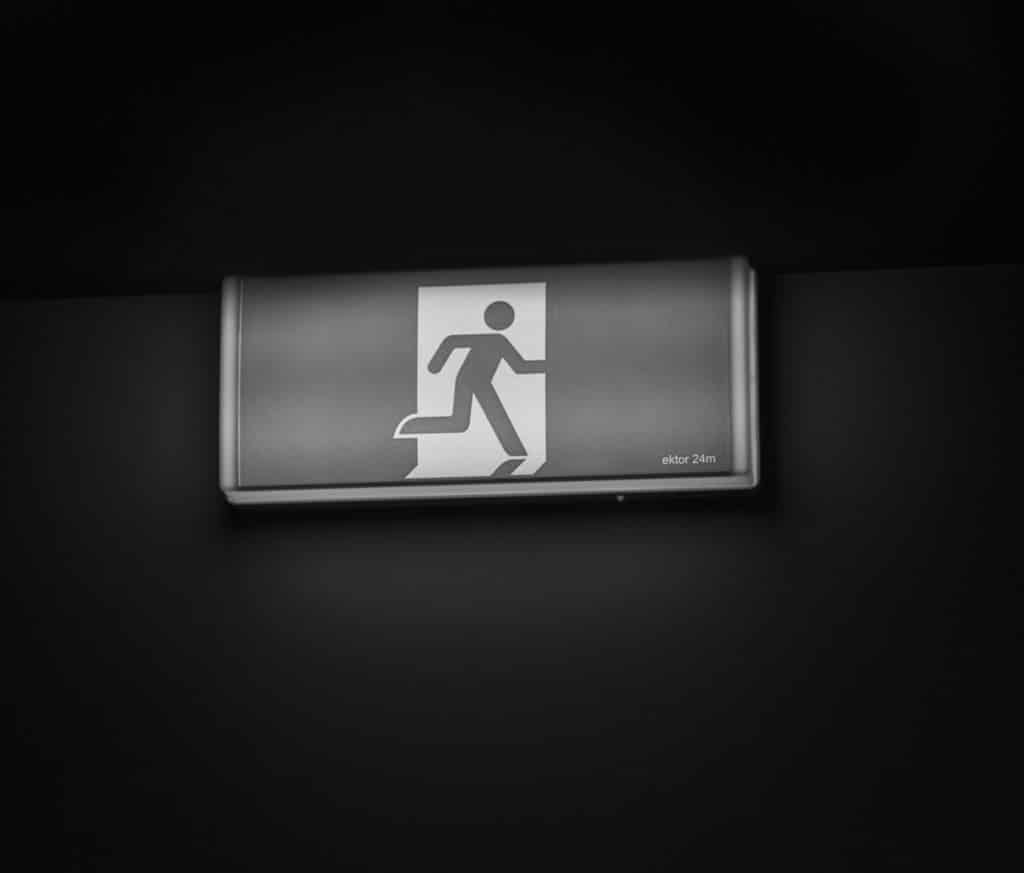 Black and white image of an exit sign hung on a plain black wall