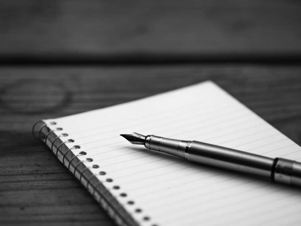 A black and white image of a notepad with a fountain pen lying on top of it